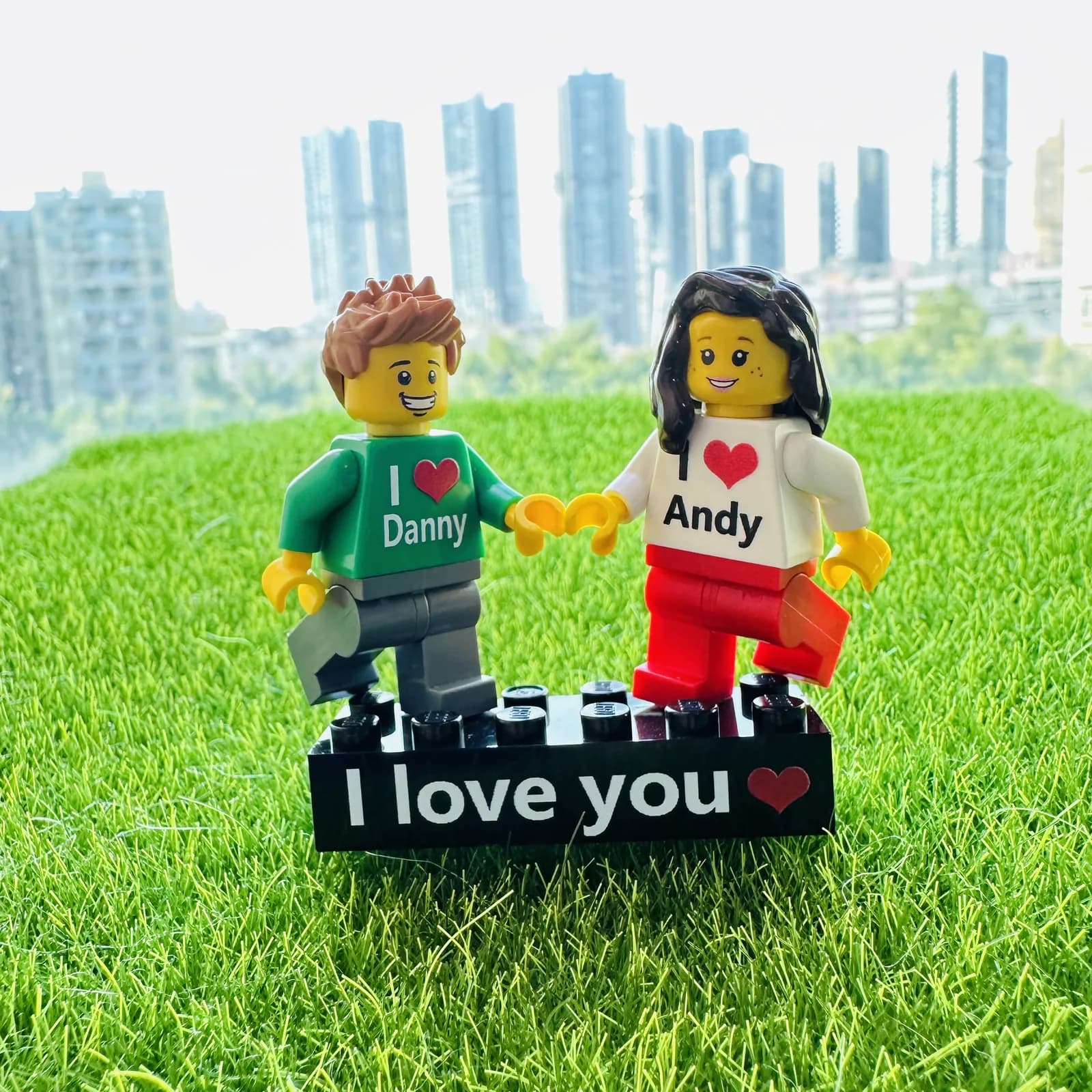 Custom couple brick figures with I love Danny and I love Andy printed on their shirts, standing on a black I love you name brick